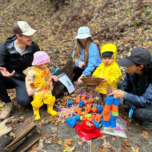 children and their parents at a play group in the woods talking and laughing